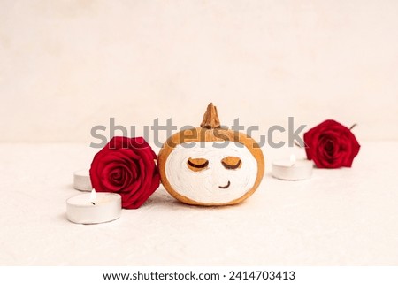 Pumpkin with drawn face, candles, roses and clay mask on light background