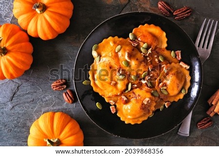 Pumpkin filled ravioli pasta with nuts and pumpkin seeds. Table scene, above view on a dark background.