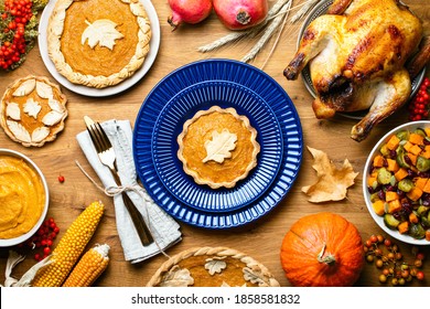 Pumpkin Mini Pie Served On A Dark Blue Plate, Top Down View Of Thanksgiving Table Setting With Various Traditional Festive Food Served For Holiday Dinner