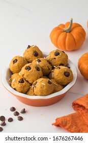 Pumpkin No Cook Protein Balls Made With Chocolate Chips. In Orange Bawl Next To Pumpkins, Orange Napkin And Chocolate Chips On White Table Top. 