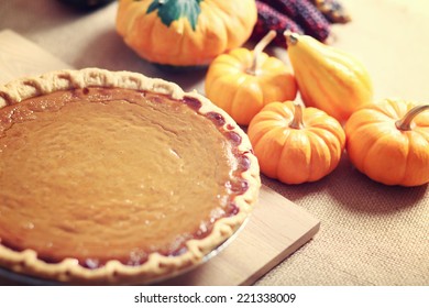 Pumpkin pie with autumn pumpkins and corn on wooden board