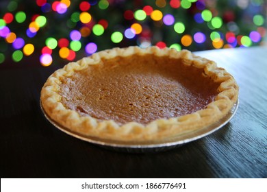 Pumpkin Pie. Fresh Baked Pumpkin Pie On A Wooden Table With Christmas Tree Lights In The Background. Pumpkin Pie Is Enjoyed World Wide For Christmas And Other Holidays. 