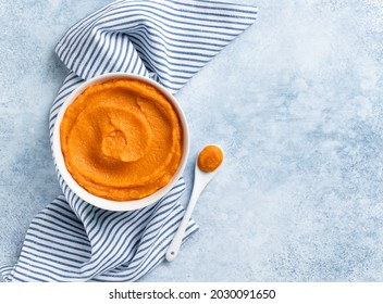 Pumpkin puree (mashed butternut squash) in white ceramic bowl top view. Blue and white stripes textile, white tea spoon. Copy space. Seasonal cooking concept. Ingredient for autumn baking.