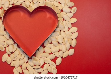 Pumpkin seeds folded in the shape of a heart, red background. - Shutterstock ID 1910473717