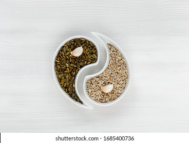 Pumpkin Seeds And Sunflower Seeds Lie On A White Background With Garlic Cloves In The Shape Of A Yin Yang Sign. The Concept Of Healthy Eating, Organic Food. The View From The Top