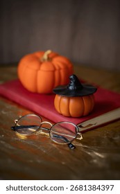 Pumpkin shaped decor on the table with black witch's hat, glasses and red notebook, bronze tablecloth, wooden background, seasonal decor, Halloween, autumn, dark photo, home decor, handmade, holiday