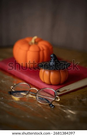 Pumpkin shaped decor on the table with black witch's hat, glasses and red notebook, bronze tablecloth, wooden background, seasonal decor, Halloween, autumn, dark photo, home decor, handmade, holiday