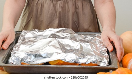 Pumpkin slices close up on a prepared baking pan covered with aluminum foil. Baking pumpkin, step by step pumpkin puree recipe, lifestyle, woman hands - Shutterstock ID 2186002055