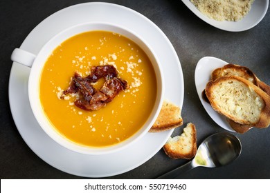 Pumpkin Soup With Bacon, Parmesan And Garlic Bread.  Top View, Over Dark Slate.