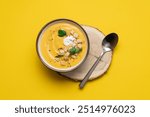 Pumpkin soup with cream and bread croutons in bowl on a yellow background. Seasonal autumn dish on the table top view