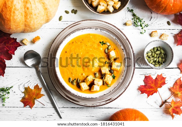 Pumpkin soup\
and organic pumpkins on white wooden table, top view. Seasonal\
autumn food - Spicy pumpkin and carrot\
soup.