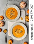 Pumpkin soup and organic pumpkins, top view, gray background. Seasonal autumn food - Spicy pumpkin soup with cream, croutons and pumpkin seeds.