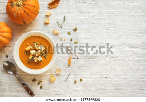 Pumpkin soup and organic pumpkins, top view, copy\
space. Seasonal autumn food - Spicy pumpkin soup with croutons and\
pumpkin seeds.