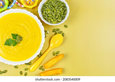 Pumpkin Soup Puree For The Baby, Pumpkin Seeds And Pieces, A Spoon And A Toy On A Yellow Background. Place For Text, Recipe. Baby Nutrition, The First Complementary Food.