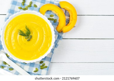 Pumpkin Soup Puree For Baby, Pumpkin Seeds And Pieces, A Spoon On A Blue Napkin And A White Wooden Background. Place For Text, Recipe. Baby Nutrition, The First Complementary Food.