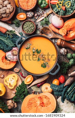 Pumpkin soup with vegetarian cooking ingredients, wooden spoons, kitchen utensils on wooden background. Top view. Vegan diet. Autumn harvest. Healthy, clean food and eating concept. Zero waste