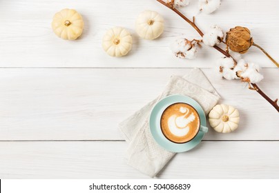 Pumpkin Spice Latte. Blue Coffee Cup With Foam, Cinnamon Sticks, Cotton Plant And Small Yellow Pumpkins At White Wood Background. Autumn Fall Hot Drinks, Cafe And Bar Concept, Top View With Copy Space