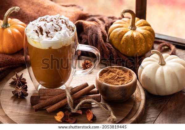 Pumpkin spice latte with cinnamon sticks on a\
wooden platter and pumpkins by a\
window