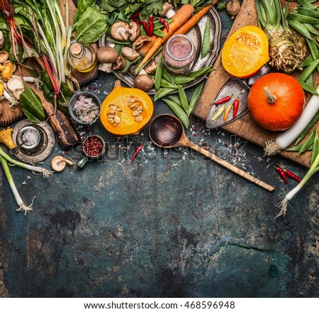 Pumpkin with vegetarian cooking ingredients, wooden spoon on dark rustic background, top view, border