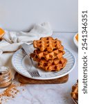 Pumpkin waffles stacked on plate with white background and marble tabletop.