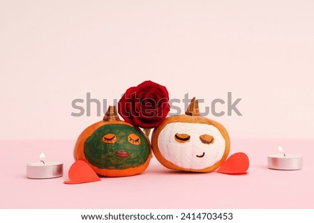 Pumpkins with drawn faces, candles, rose, paper hearts and clay masks on pink background