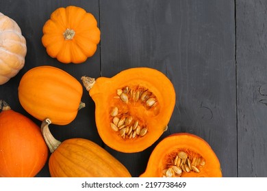 Pumpkins in the kitchen. Cut orange Hokkaido pumpkin with seeds on black wooden background.