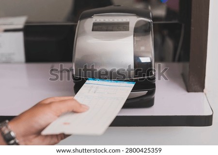 Punch card time clock machine processing attendance card in office setting, recording work hours and supporting workforce tracking and payroll accuracy.