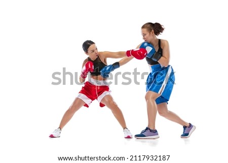 Punch. Dynamic portrait of two female professional boxers boxing isolated on white studio background. Two muscular athletes in boxing gloves sparring. Sport, competition, show, power, action concept.