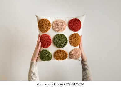 Punch needle embroidery pillow diy. Close up of woman hands holding pillow. Product is made according to the technique pushing woolen threads on foundation fabric with needle with wood handle  - Shutterstock ID 2108475266
