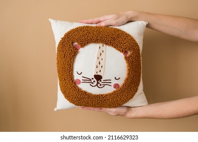 Punch needle embroidery pillow diy. Close-up of  hands holding pillow according to  technique pushing woolen threads on foundation fabric with needle with wood handle according to pattern