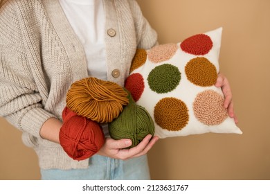 Punch needle embroidery pillow diy. Close-up of woman hands holding pillow. Product is made according to the technique pushing woolen threads on foundation fabric with needle with wood handle