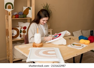 Punch needle embroidery. Young woman pushing the punchneedle straight down into the foundation fabric in workshop. Female embroidering handmade picture rainbow on canvas. Handicraft, hobby, diy