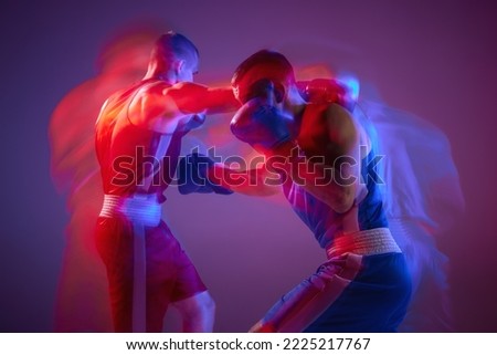 Punch. Unfocused effect portrait of two professional boxers boxing isolated on purple background in neon light. Concept of sport, competition, training, energy. Copy space for ad, text