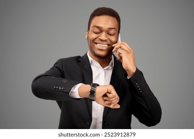 Punctuality Concept. Happy african manager checking time on wrist watch while talking on smartphone, empty space - Powered by Shutterstock