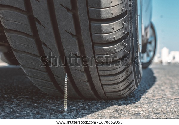 puncture wheel concept. the self-tapping screw lies\
on asphalt under a car\
wheel