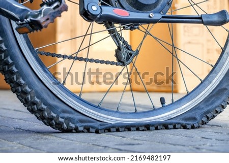 A punctured bicycle tire in selective focus against a background yellow sunlit wall in blur.