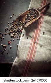 Pungent Spicy Dried Peppercorns In Assorted Black, Red And White Spilling Out Of An Old Wooden Scoop Onto A Kitchen Counter, Overhead View With Copyspace On A Kitchen Cloth