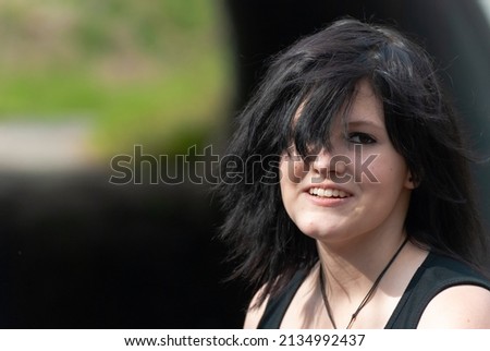 Punk emo girl, young adult with black hair and eyeliner, smiling, looking at camera, outdoors, horizontal, close-up