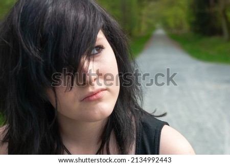 Punk emo girl, young adult with black hair and eyeliner, looking away, outdoors, close-up, horizontal
