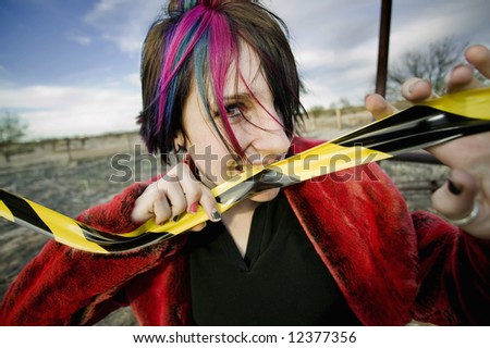 Punk girl outdoors biting a strip of yellow and black caution tape
