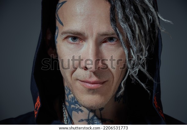 Punk and rock culture. A\
mature brutal man with ethnic tattoos and punk-style Mohawk\
dreadlocks stands with a hood on his head and looks directly at the\
camera.