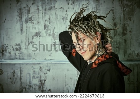Punk and rock culture. Portrait of a  mature brutal man with ethnic tattoos and punk-style Mohawk dreadlocks in black clothes with a hood looking at the camera and smiling. Copy space.