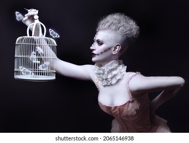 Punk Woman With Marbled skin In Beautiful Lingerie With Fluttering Butterflies In A Cage In Darkness. Souls Breaks Free From Cage.