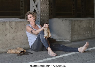 A Punk Woman Under A Bridge With Bottles Of Alcohol Nearby And A Bottle In A Brown Paper Bag In Her Hand 