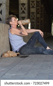 A Punk Woman Under A Bridge Drinking Alcohol Out Of A Bottle In A Brown Paper Bag