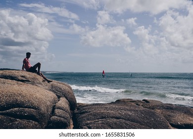 Punta Del Diablo, Uruguay / 02 05 2020: Man On The Rocks And Windsurf