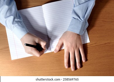 Pupil Boy At A Desk Writing In A Exercise Book. Top View.