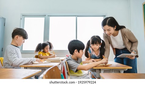 Pupil boy hi five with asian teacher in classroom at elementary school. Student boy study in primary school. Children writing notes in classroom. Education knowledge successful teamwork concept banner