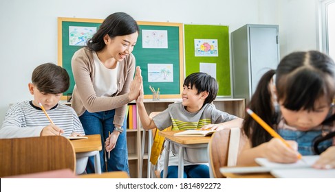 Pupil boy hi five with teacher in classroom at elementary school. Student boy studying in primary school. Children writing notes in classroom. Education knowledge, successful teamwork concept