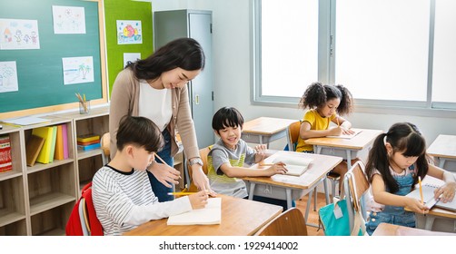 Pupil boy hi five with teacher in classroom at elementary school. Student boy studying in primary school. Children writing notes in classroom. Education knowledge, successful teamwork concept banner - Shutterstock ID 1929414002